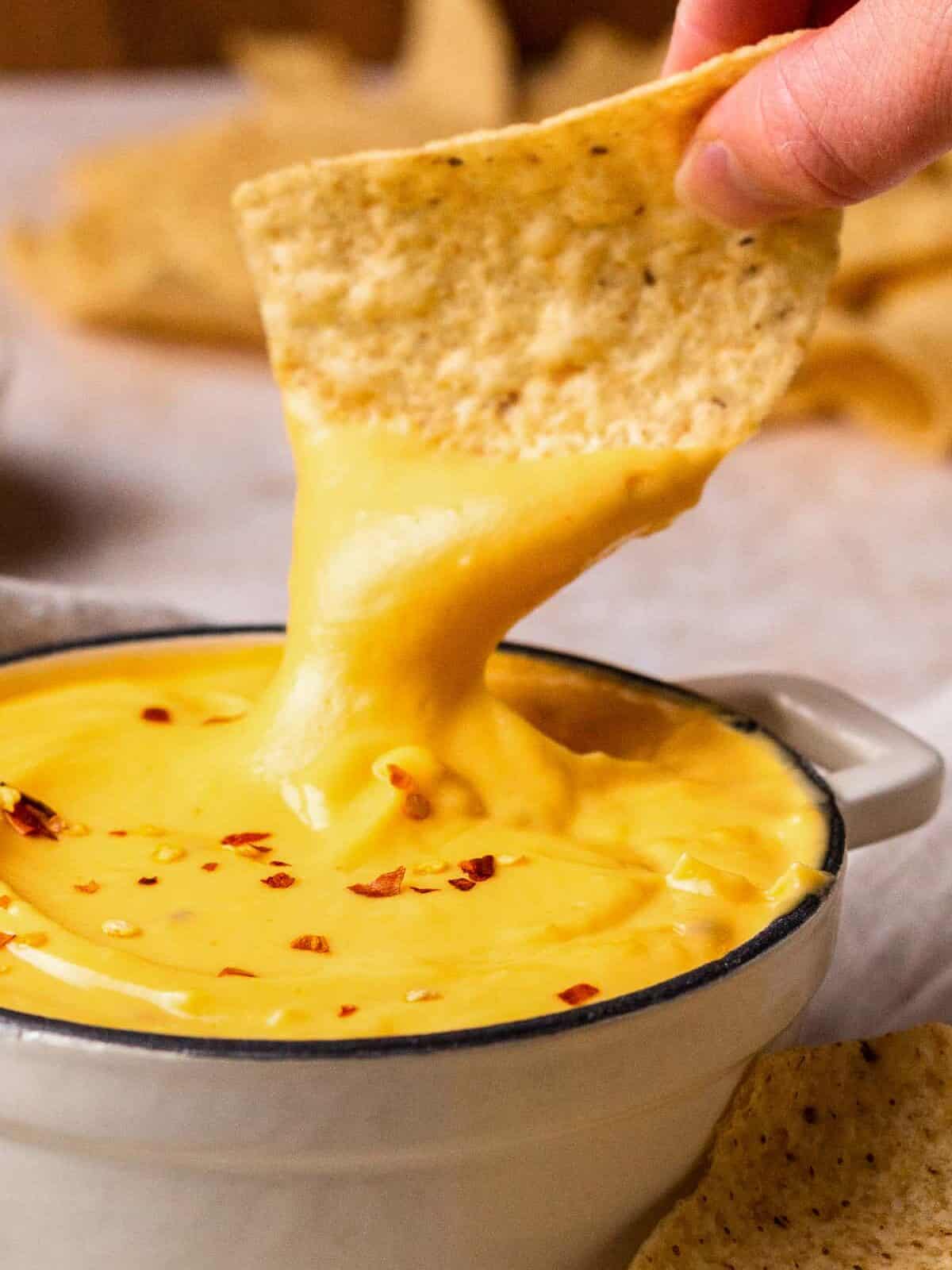 dipping a tortilla chip into nacho cheese sauce