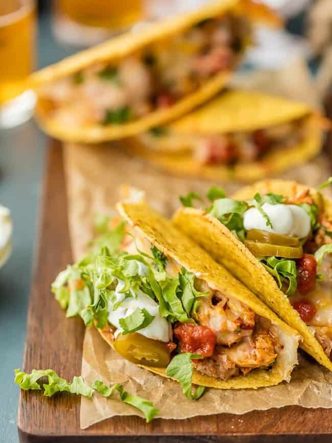 baked chicken tacos filled with shredded chicken, lettuce, and jalapeños, laid on a wooden cutting board