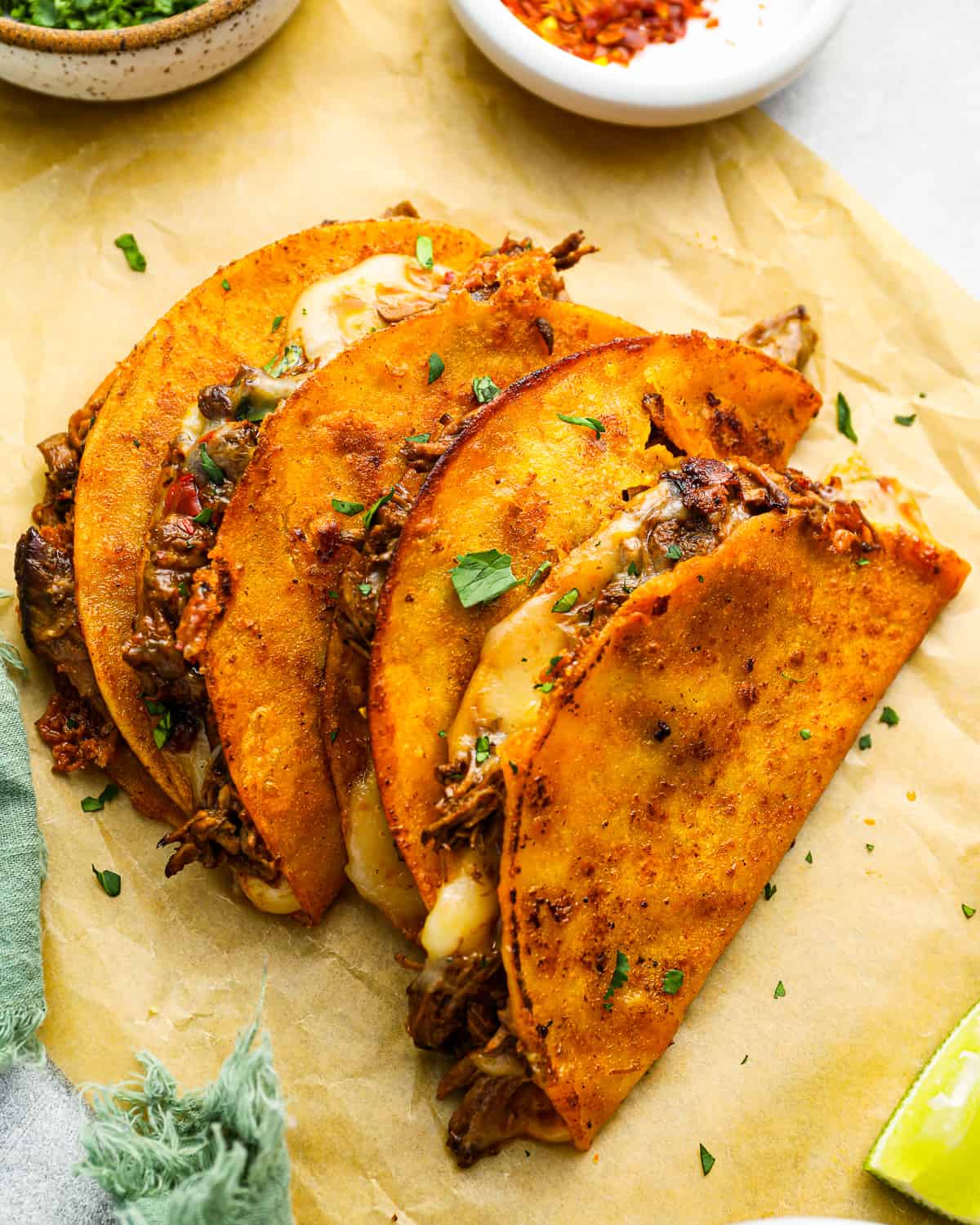 overhead view of 4 quesabirria tacos leaning against one another on parchment paper.
