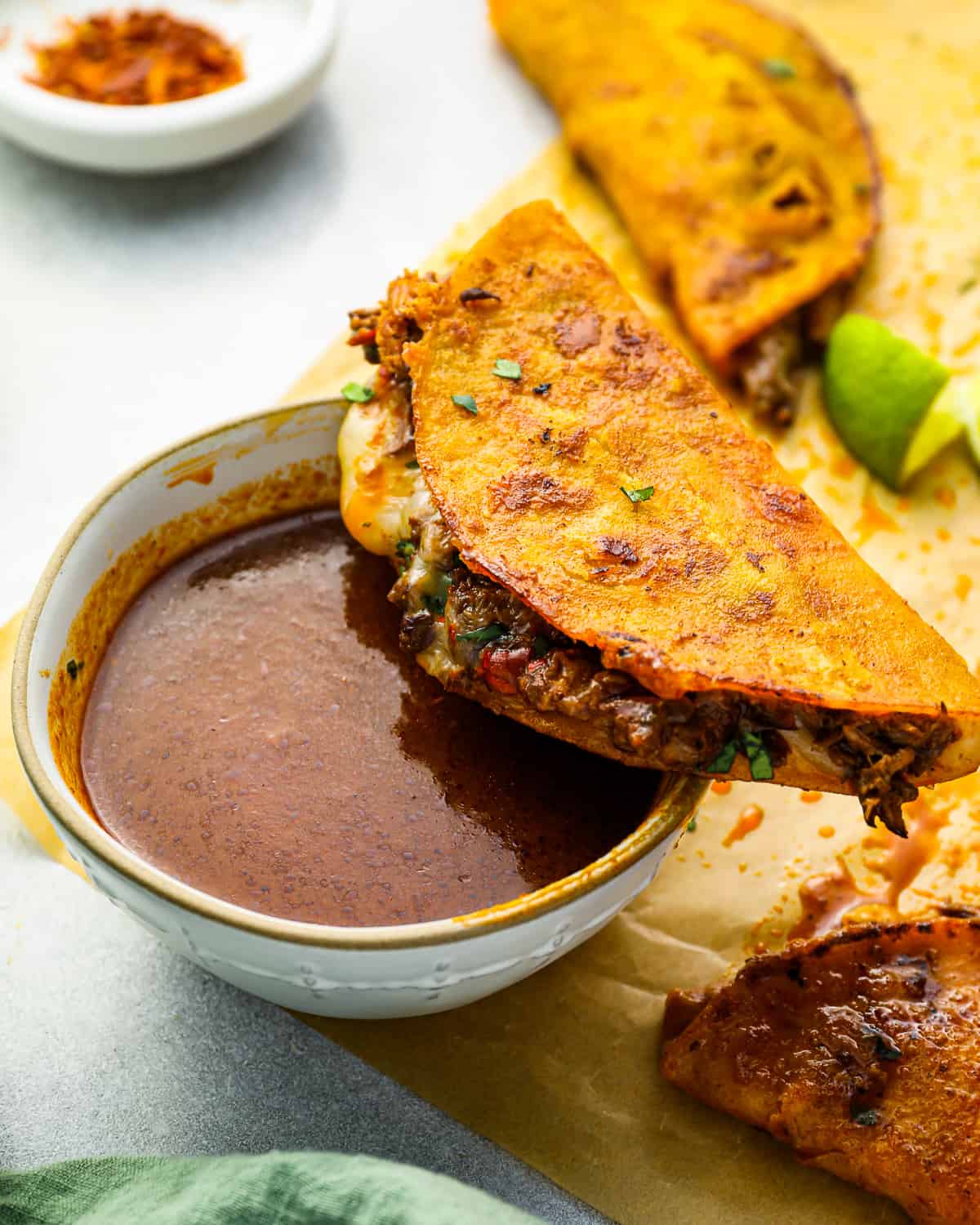 three-quarters view of a quest birria taco balanced on a cup of consomé.