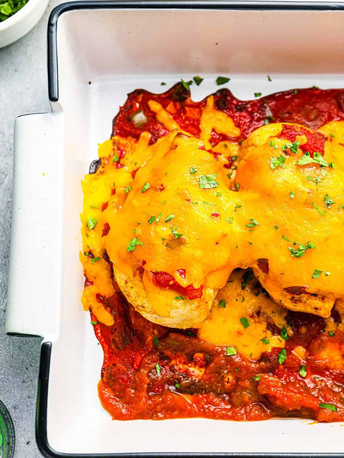 partial overhead view of baked salsa chicken in a white rectangular baking pan.