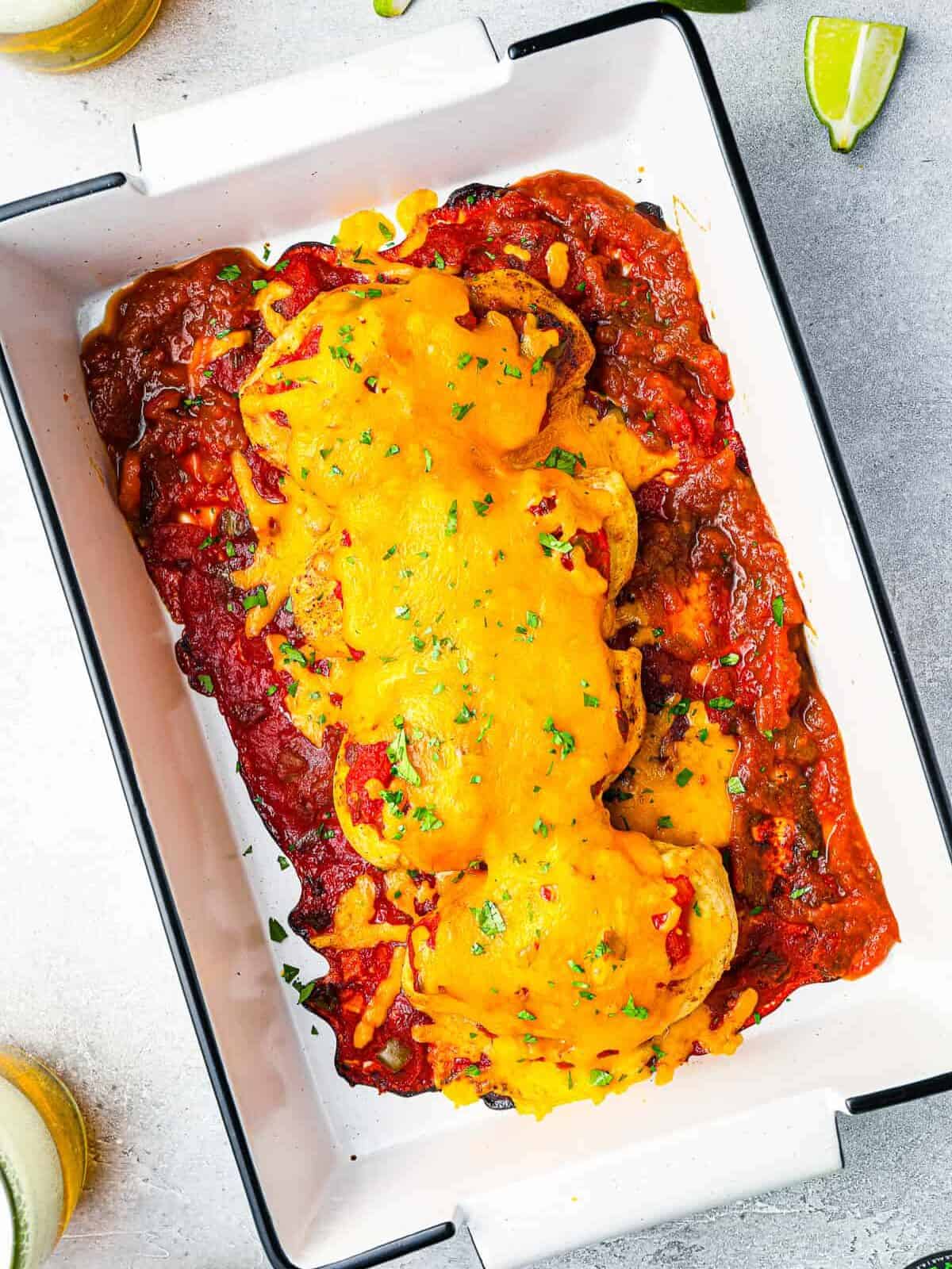 overhead view of salsa chicken topped with cheese in a white rectangular baking pan.