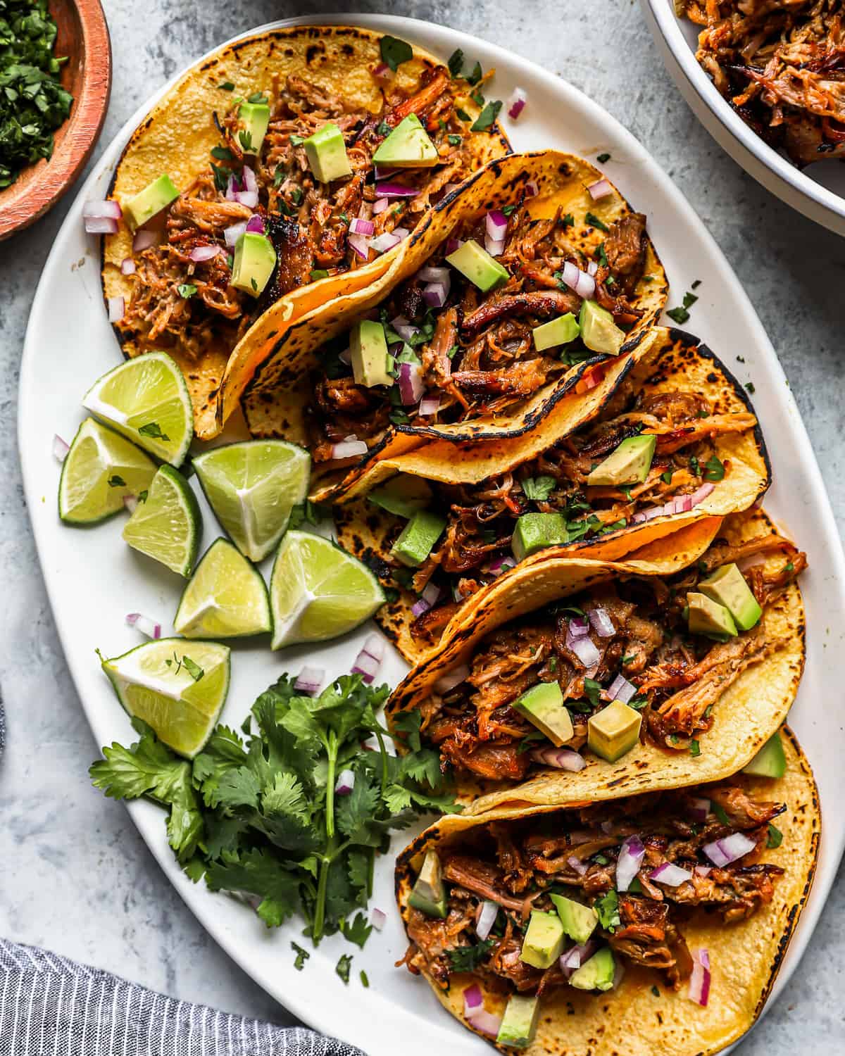 overhead view of 5 pork carnitas tacos on a white oval serving platter with limes.