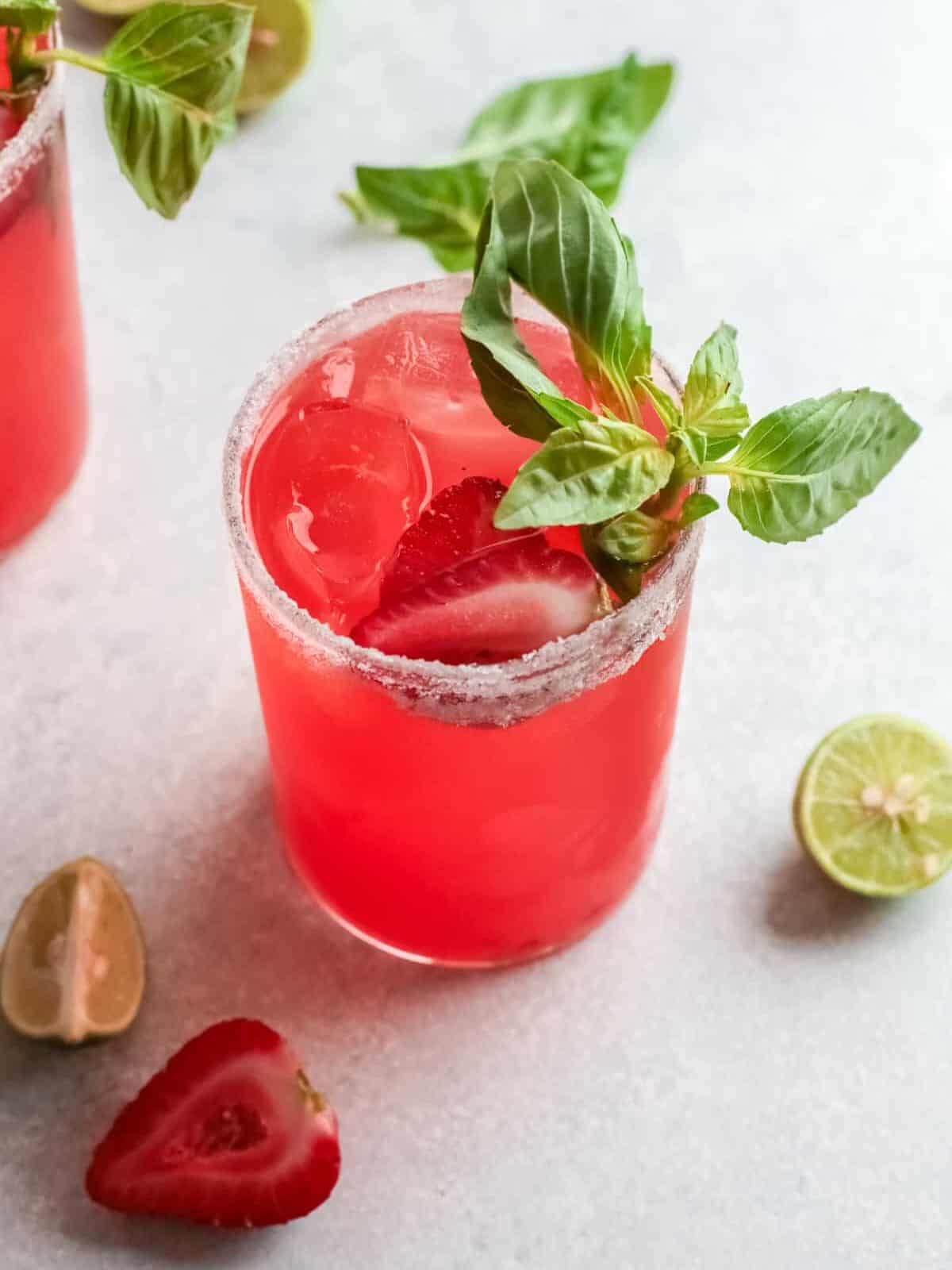 three-quarters view of a strawberry basil margarita garnished with basil and strawberries.