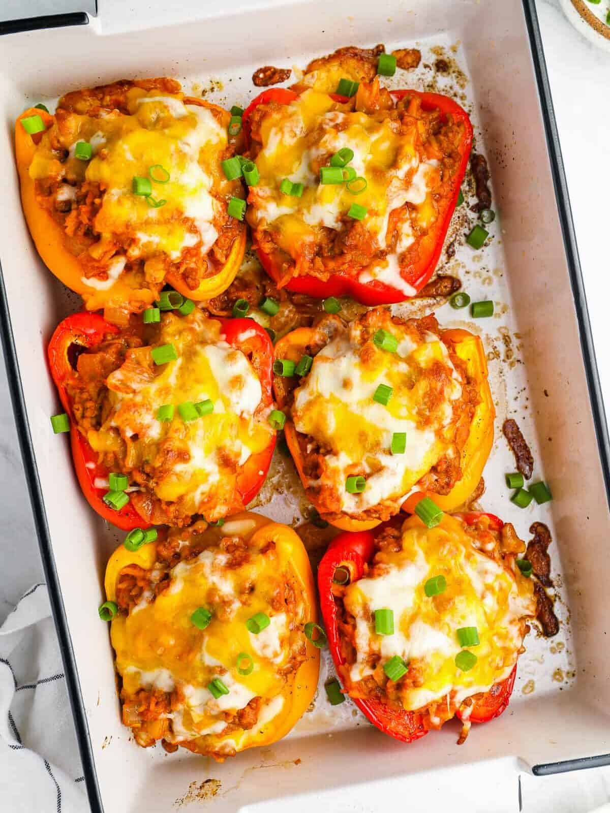 overhead view of 6 stuffed peppers in a white rectangular baking pan.