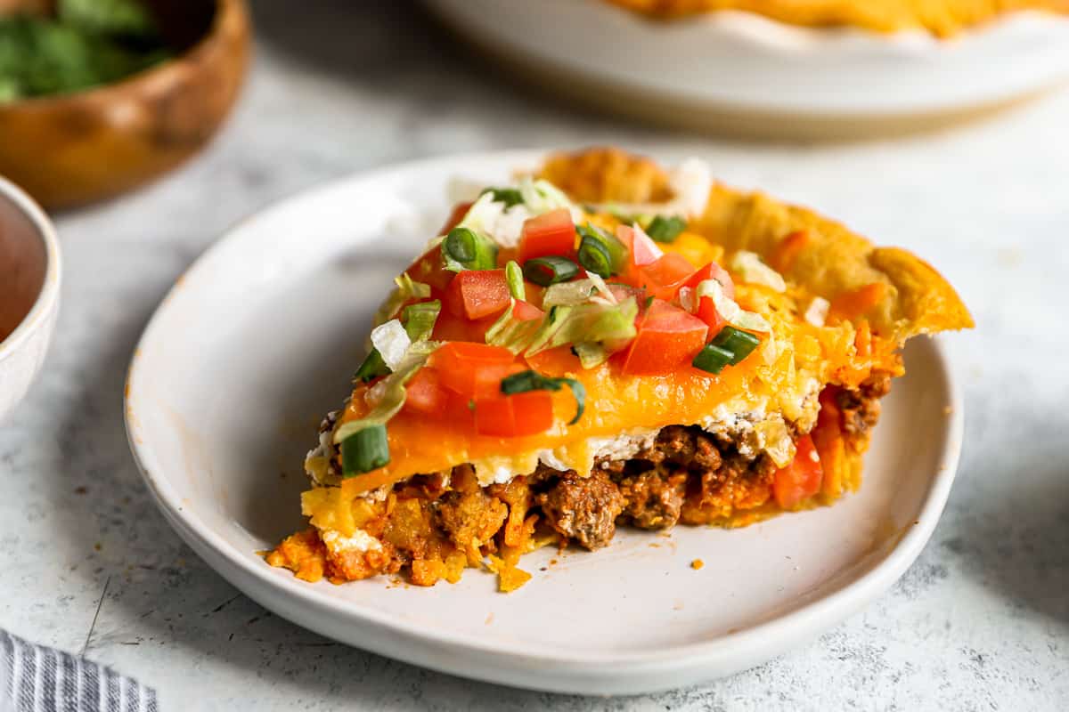 three-quarters view of a slice of taco pie on a white plate, with the ground beef filling visible from the side