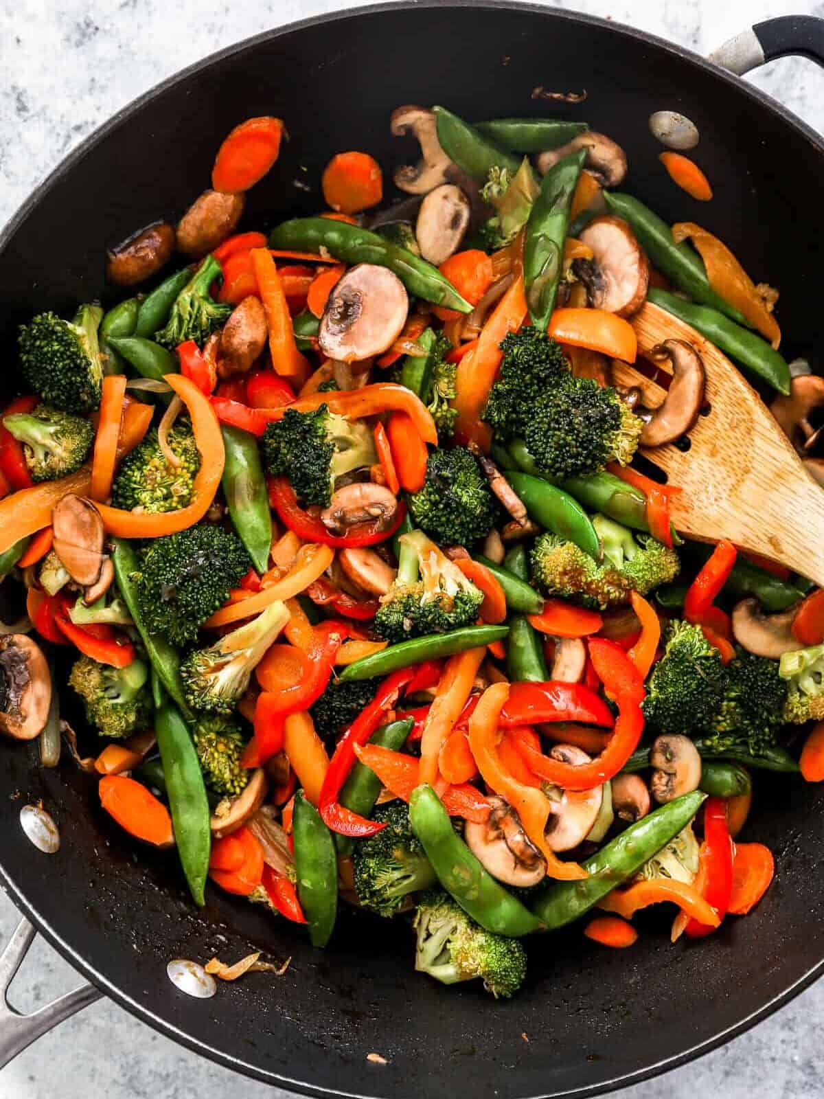 overhead view of cooking vegetable stir fry in a wok with a wooden spoon.