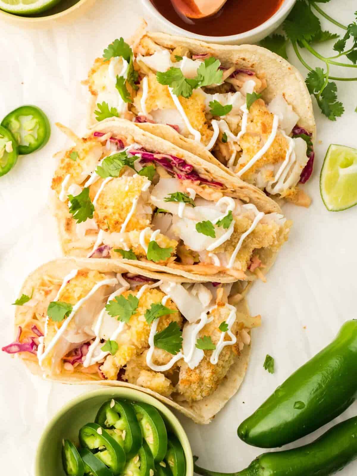 overhead view of 3 folded air fryer fish tacos on a white table.