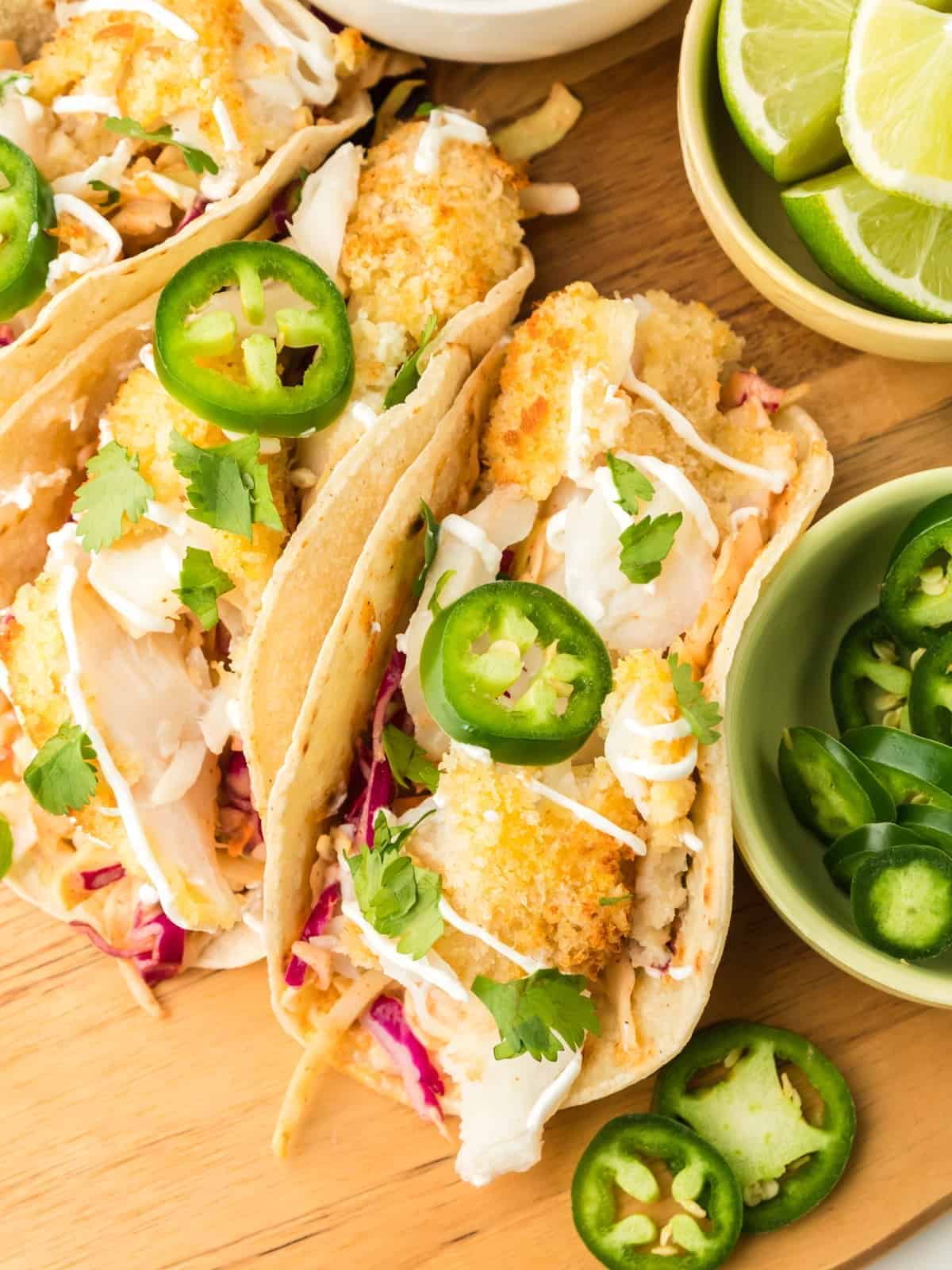 overhead view of 3 air fryer fish tacos on a wooden cutting board with sliced jalapeños.