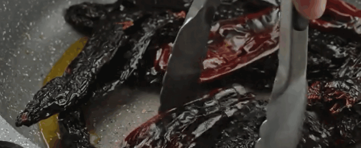 Dried chili peppers cooking in oil in a skillet.