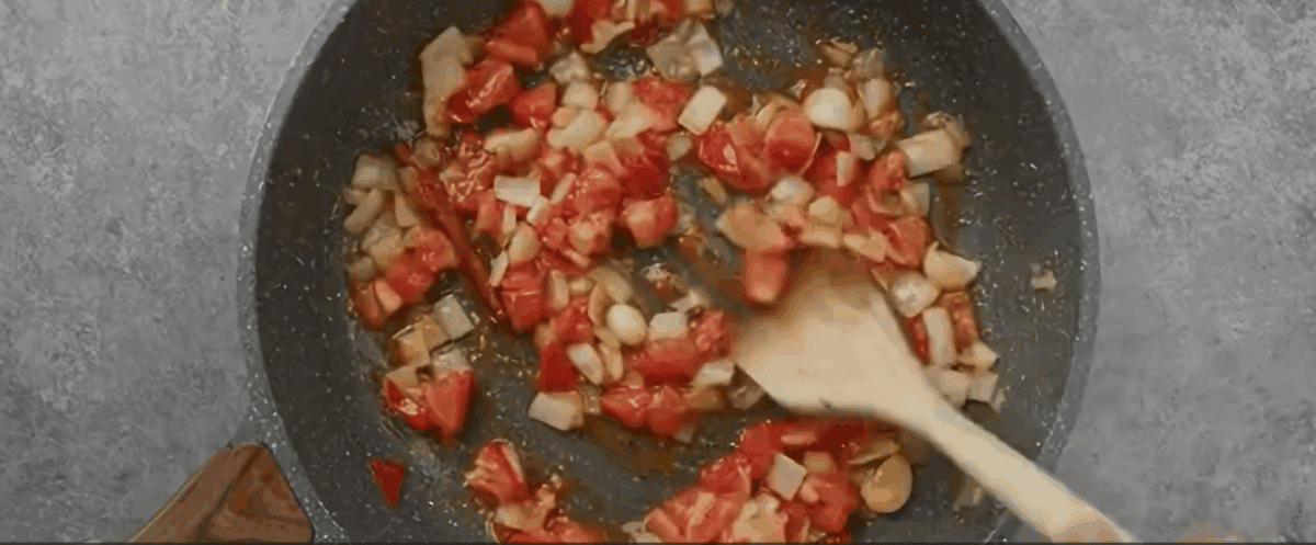 Sauteeing onion, tomatoes, garlic, cinnamon and cloves in a skillet.
