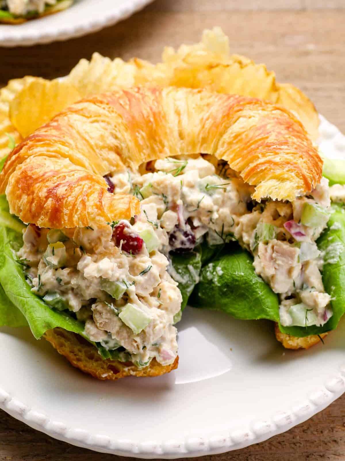 chicken salad on a croissant on a white plate with potato chips.