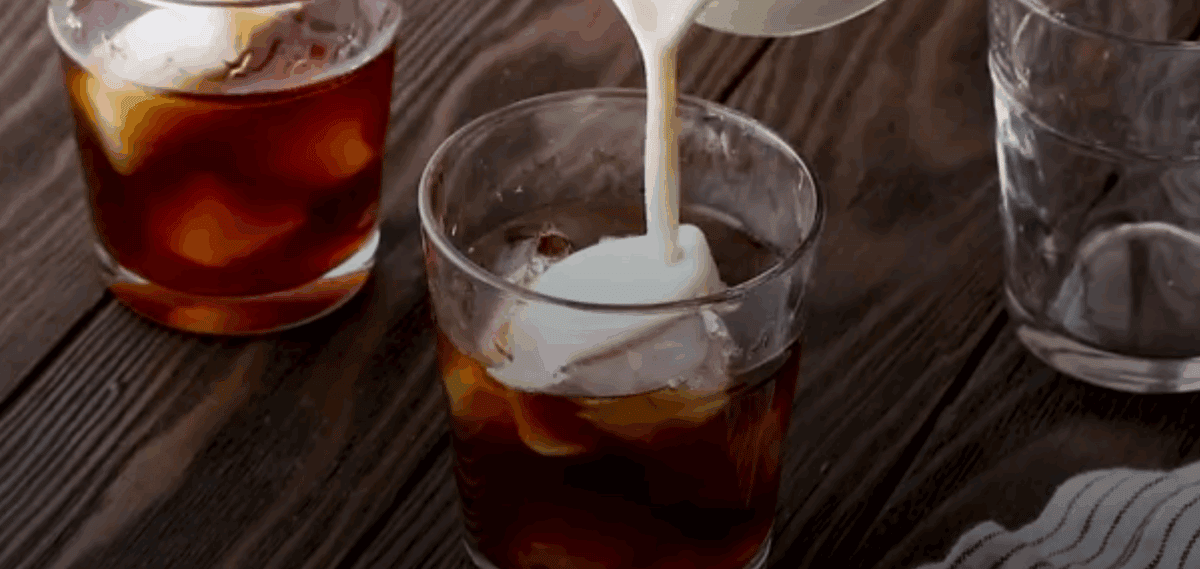 Pouring the coffee creamer into a glass of iced coffee. 