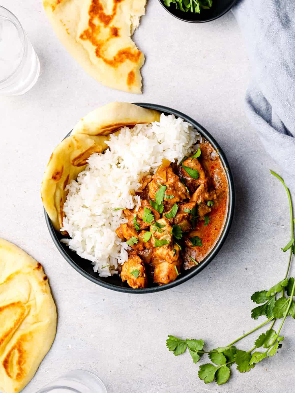 overhead view of crockpot chicken tikka masala with rice and naan in a black bowl.