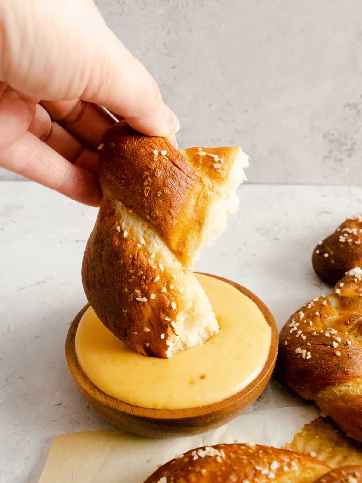 a hand dipping a homemade pretzel into cheese sauce.