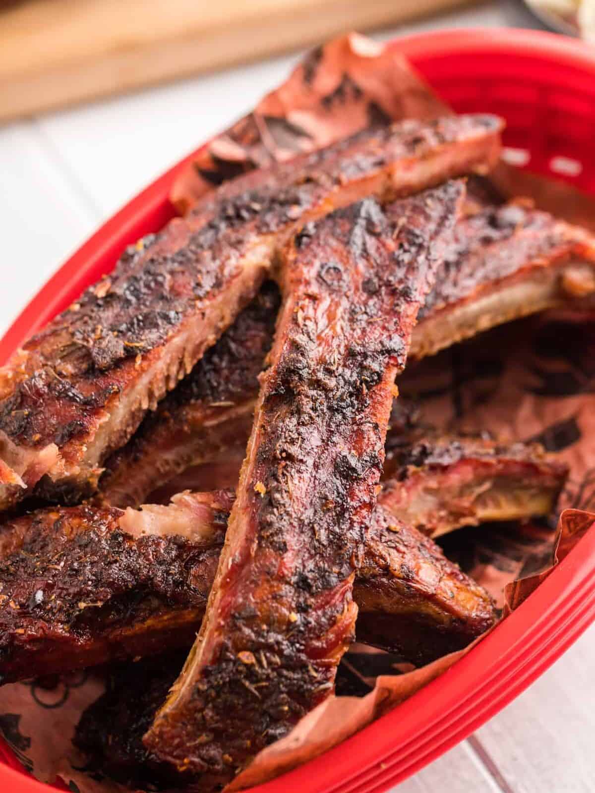 three-quarters view of smoked ribs in a red plastic basket.