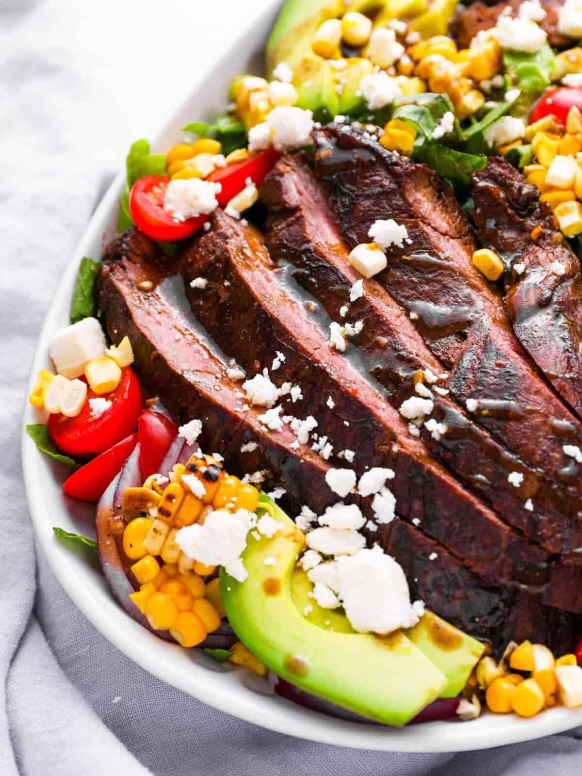 partial overhead view of steak salad in a white oval serving platter.