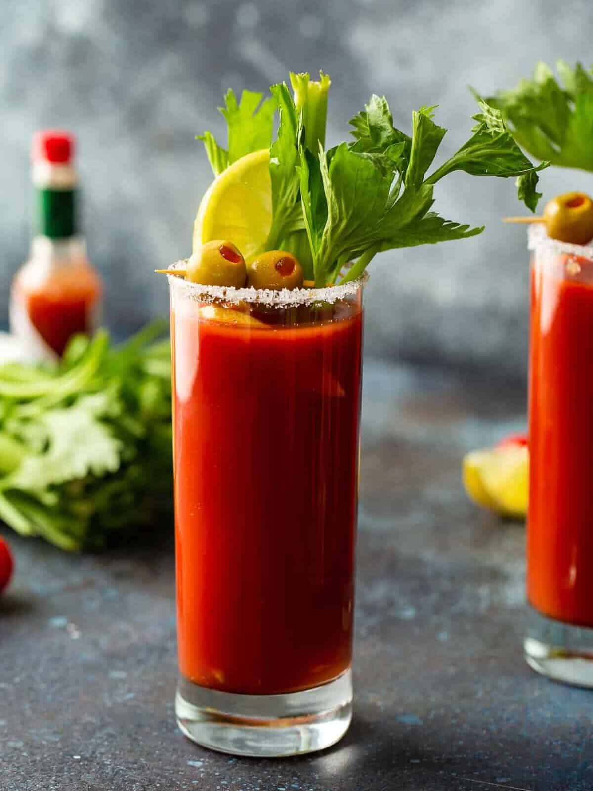 Side view of a bloody mary in a glass with a salt rim and garnishes.