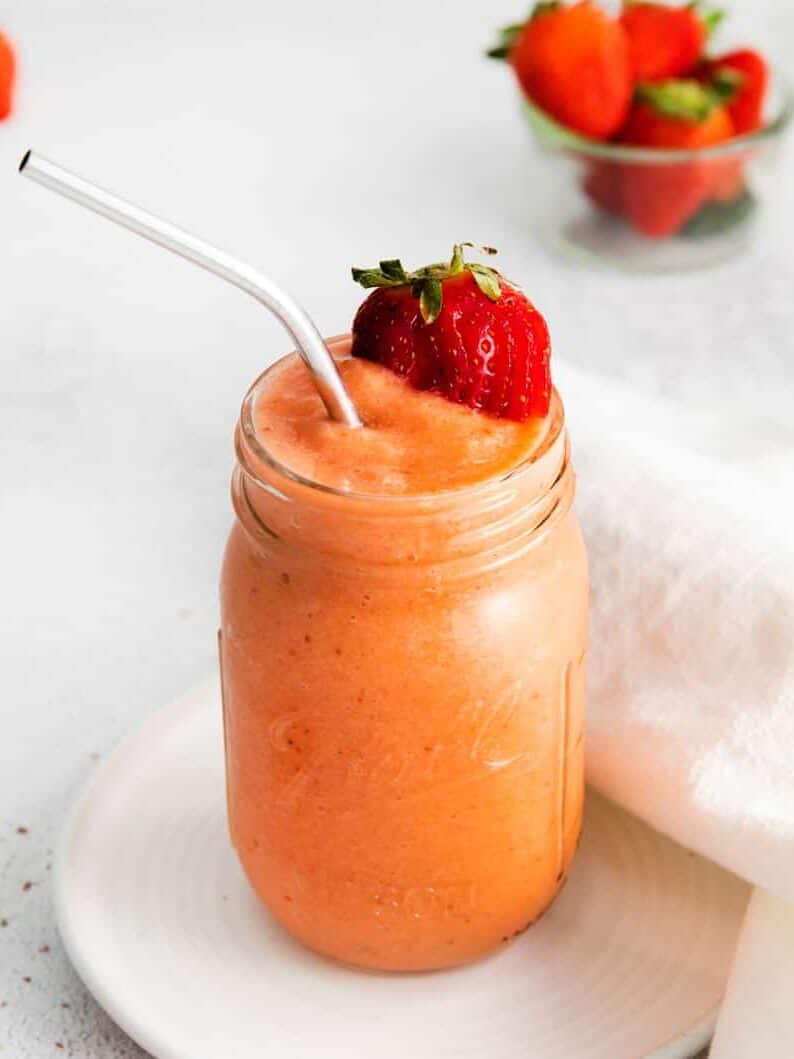 three quarters view of a strawberry mango smoothie in a mason jar with a stainless steel straw.