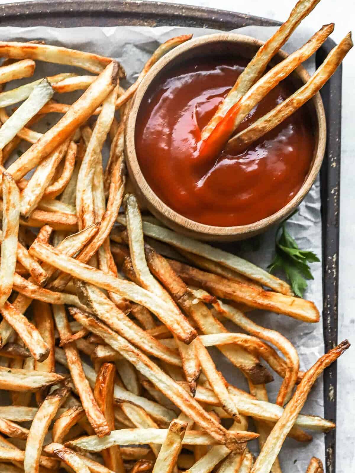 partial overhead view of air fryer french fries on a baking sheet with a cup of ketchup.
