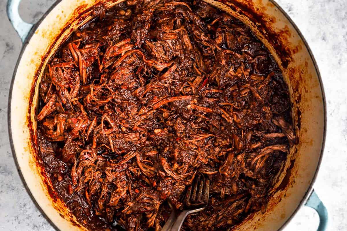 overhead view of shredded birria taco meat in a blue and white dutch oven.