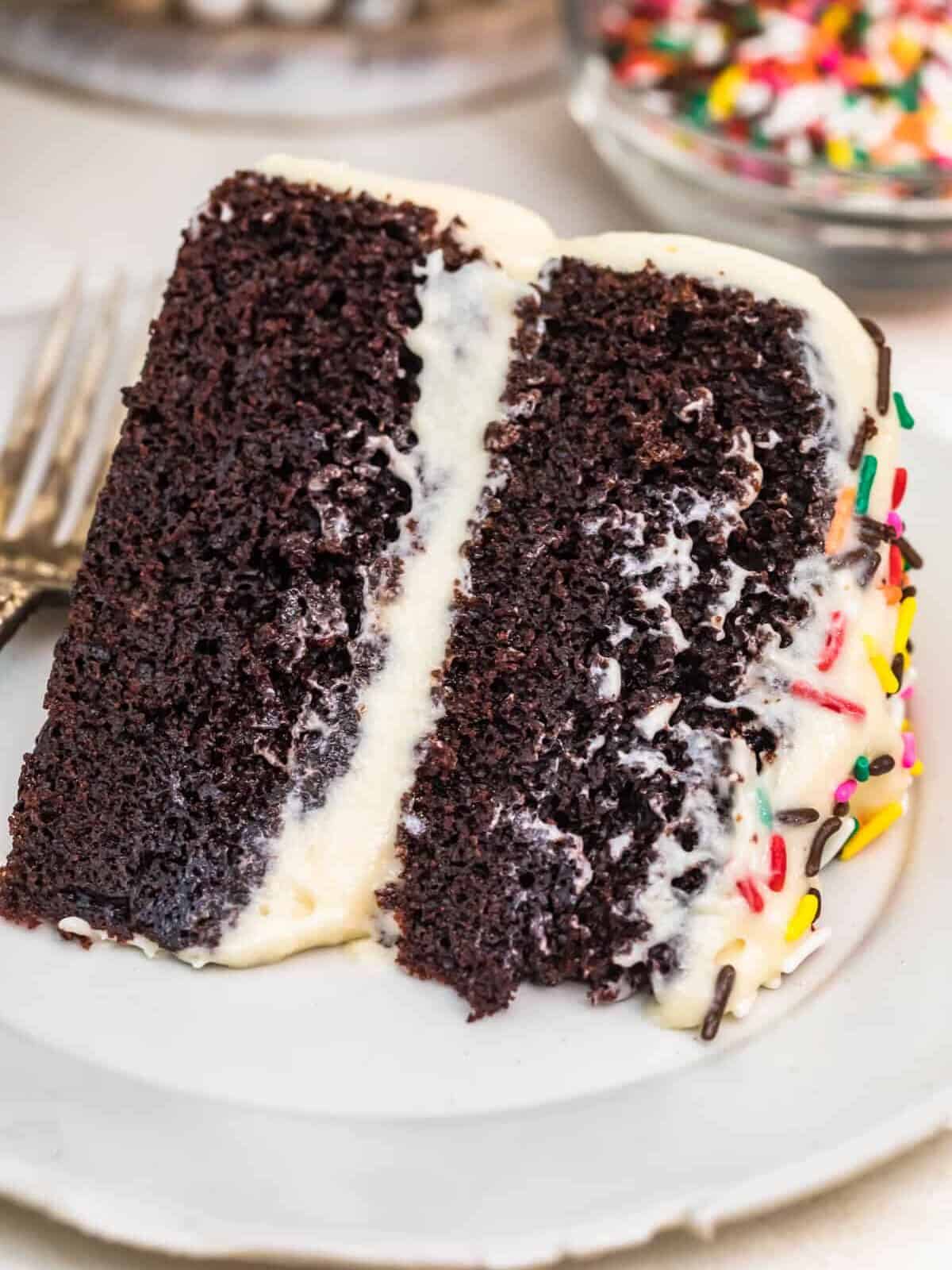 A piece of chocolate cake on a plate, with Icing and Cookie