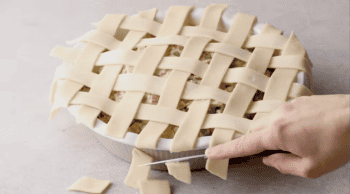cutting lattice pie crust strips to fit over chicken pot pie filling in a pie dish.