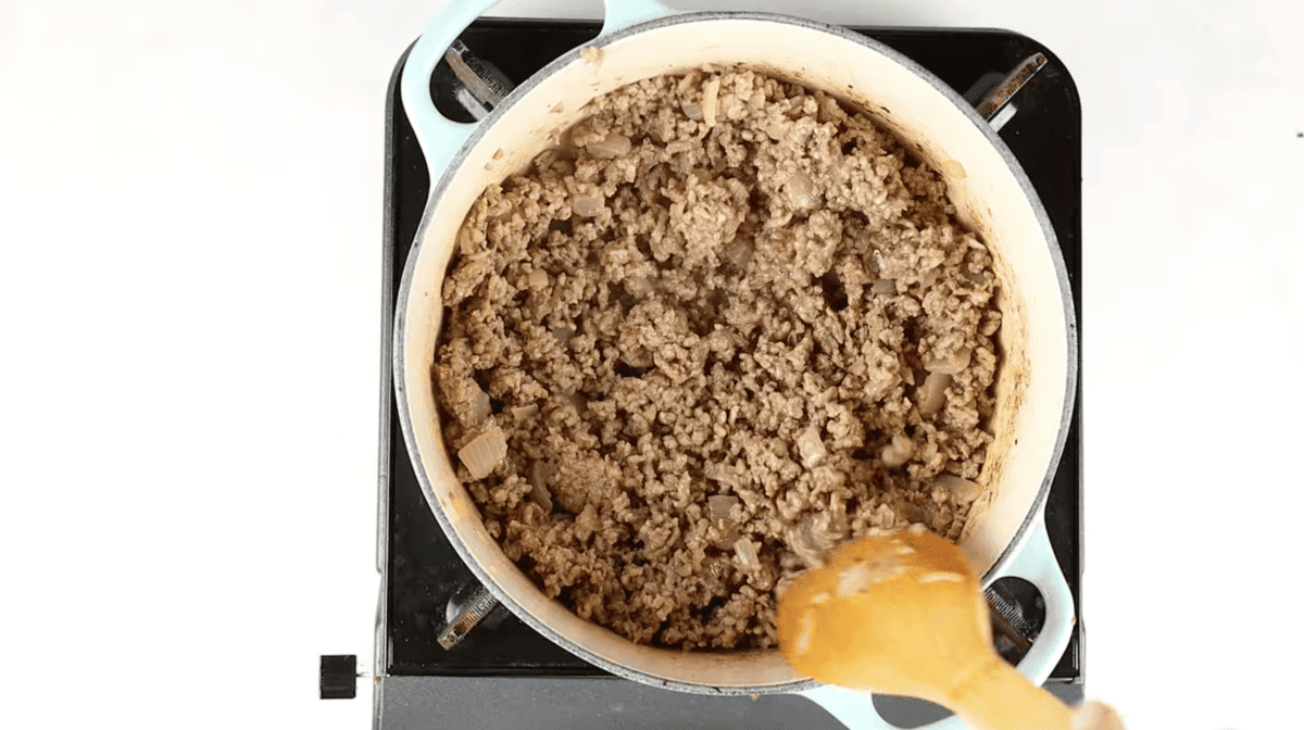 A person pouring a spoonful of chili into a pan.