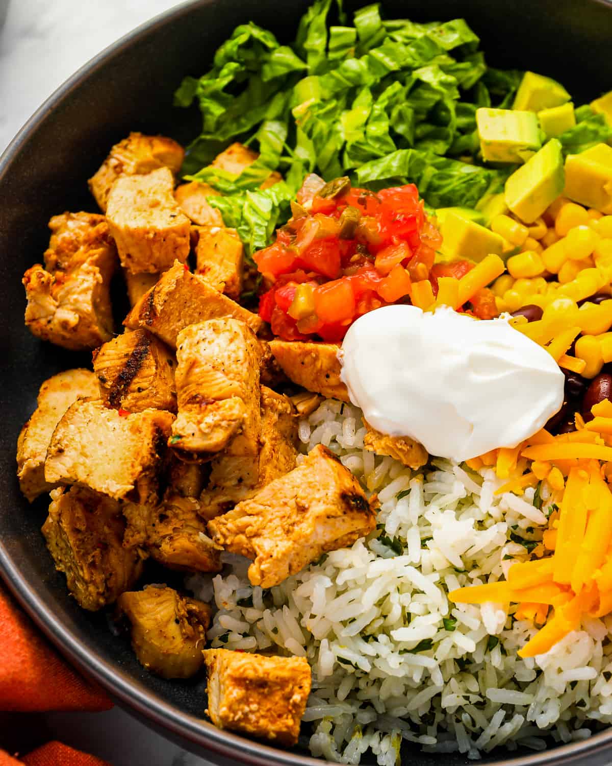 close up on a bowl filled with marinated chicken, cilantro lime rice, cheese, and other burrito ingredients.