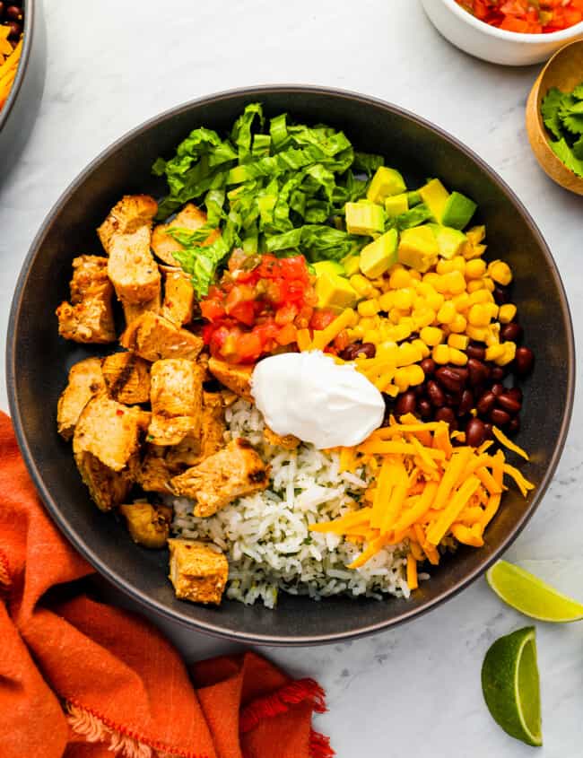 a bowl of mexican rice with chicken, corn, beans and sour cream.