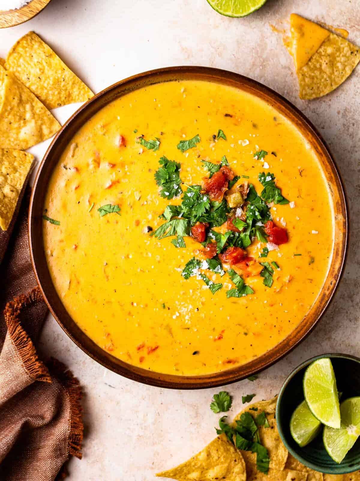 overhead view of a bowl of crockpot queso cheese dip garnished with tomatoes and cilantro, with scattered tortilla chips laid around it
