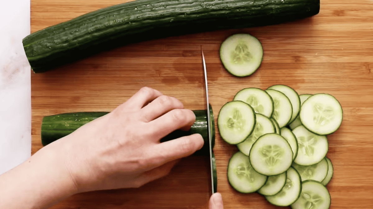 cutting cucumbers into thin slices on a wooden cutting board.