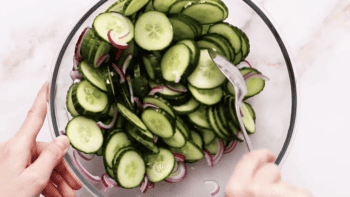 Sliced cucumbers and red onion mixed in a glass bowl.