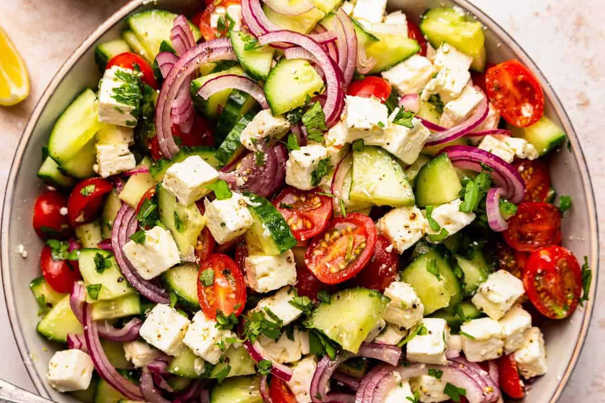 sliced cucumbers, tomatoes, feta, and red onion piled up in a large bowl