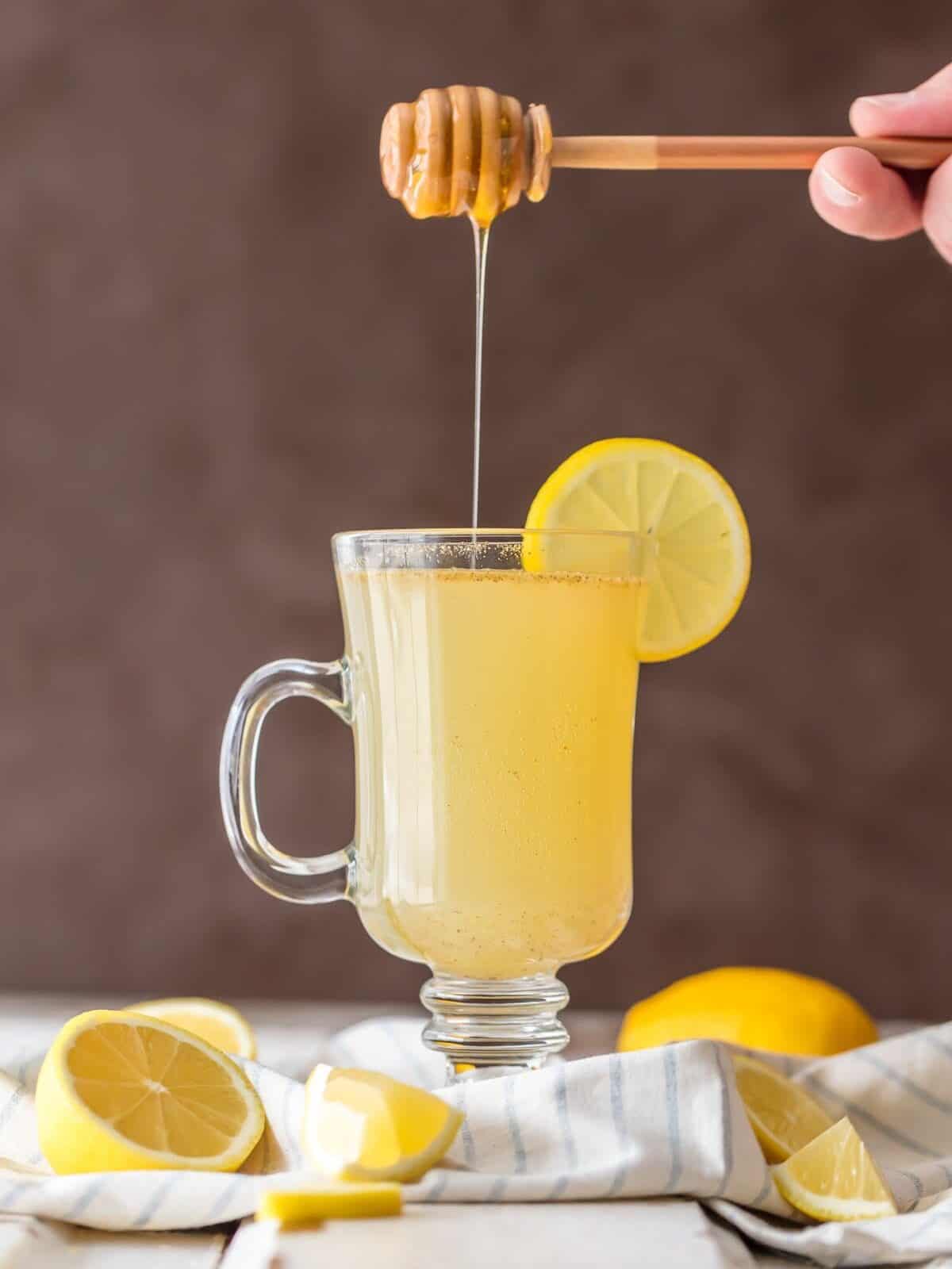 drizzling honey over master cleanse lemon detox water in a clear mug with a lemon slice.