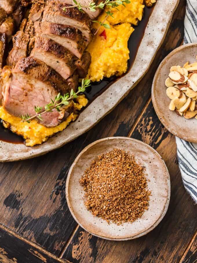 a bowl of pork seasoning next to a large platter of pork tenderloin