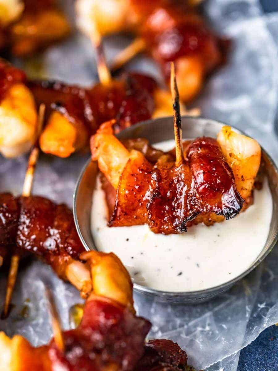 close up on a bacon wrapped shrimp dipped in a small bowl of ranch