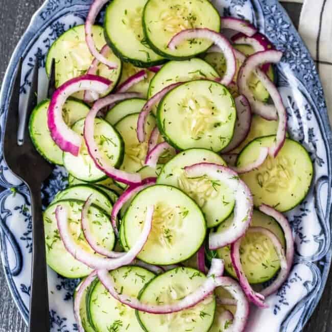 cucumber salad with red onion and dill on a blue and white plate.