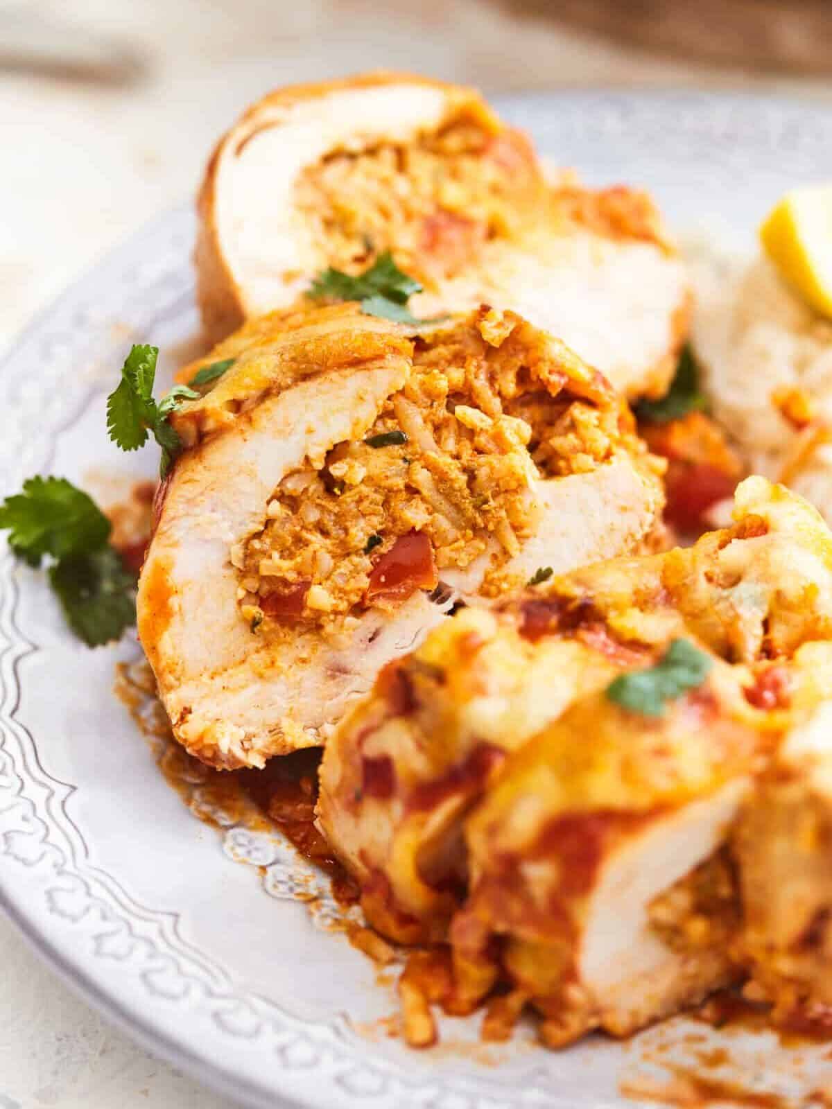 three-quarters view of a cut enchilada stuffed chicken breast on a white plate.