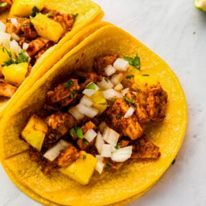 two tacos with chicken and pineapple on a plate.