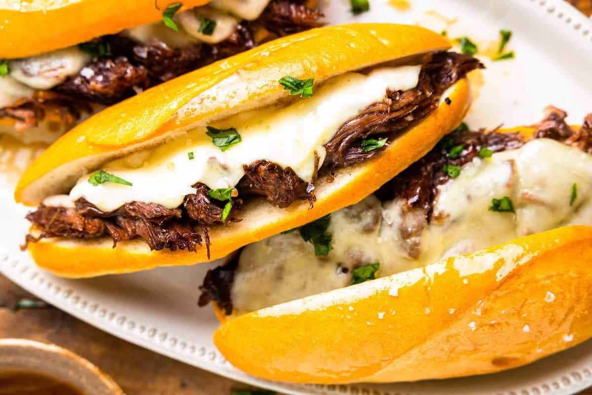 overhead view of 3 crockpot french dip sandwiches on a white oval serving tray.