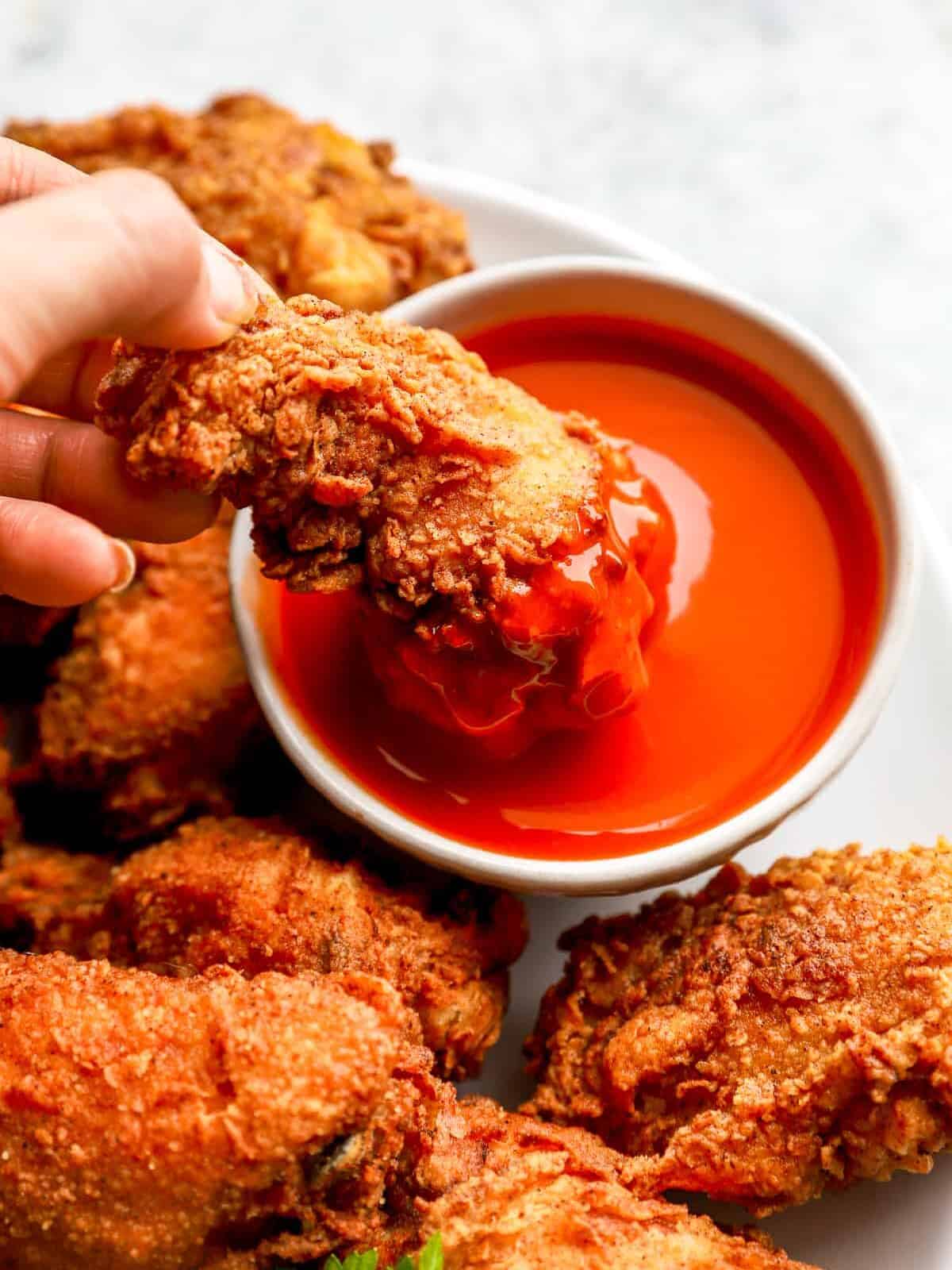 a hand dipping a fried chicken wing into a bowl of buffalo sauce.