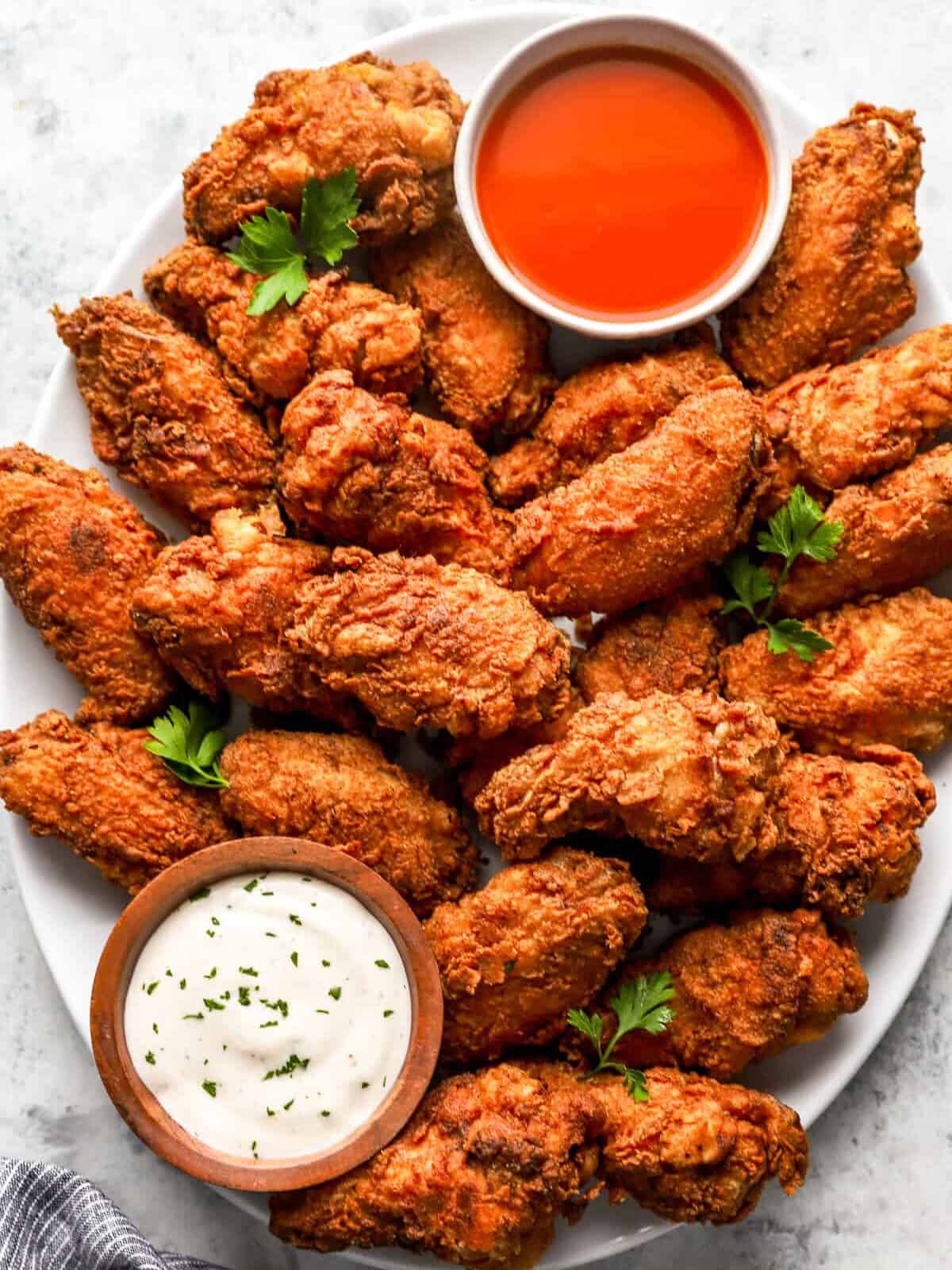 overhead view of fried chicken wings on a white platter with buffalo sauce and ranch.