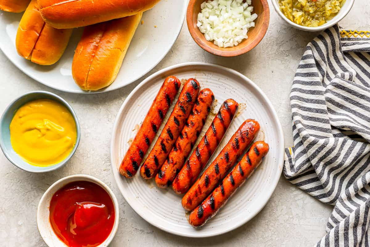 overhead view of 6 grilled hot dogs on a white plate.