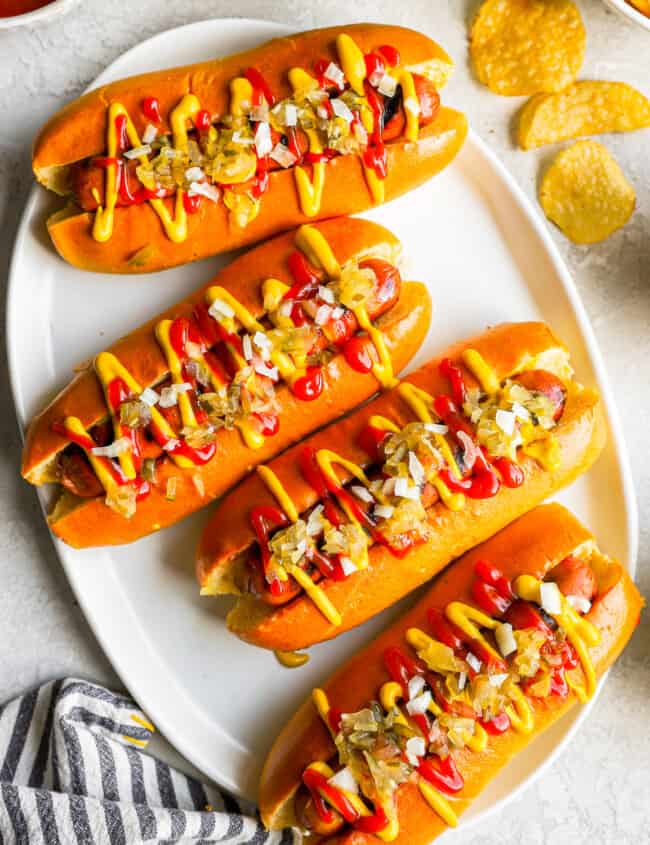 overhead view of 4 topped hot dogs on a white plate.