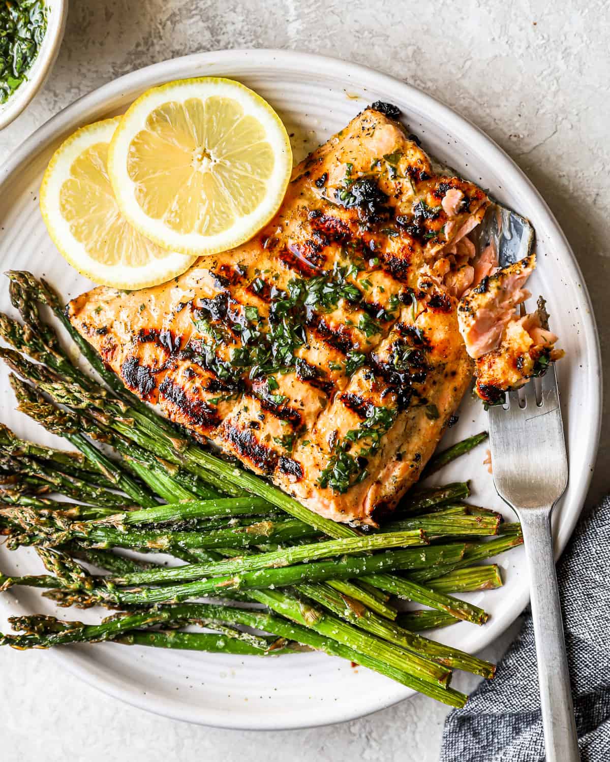 overhead view of a partially eaten grilled salmon fillet on a white plate with asparagus, lemon slices, and a fork.