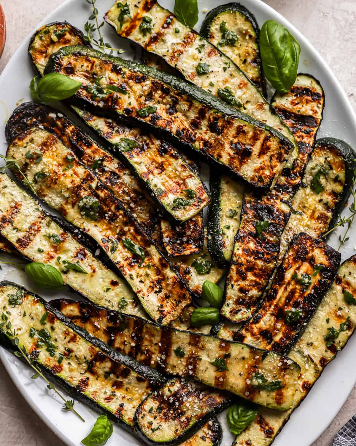 close up view of char-grilled zucchini strips on a white oval plate.