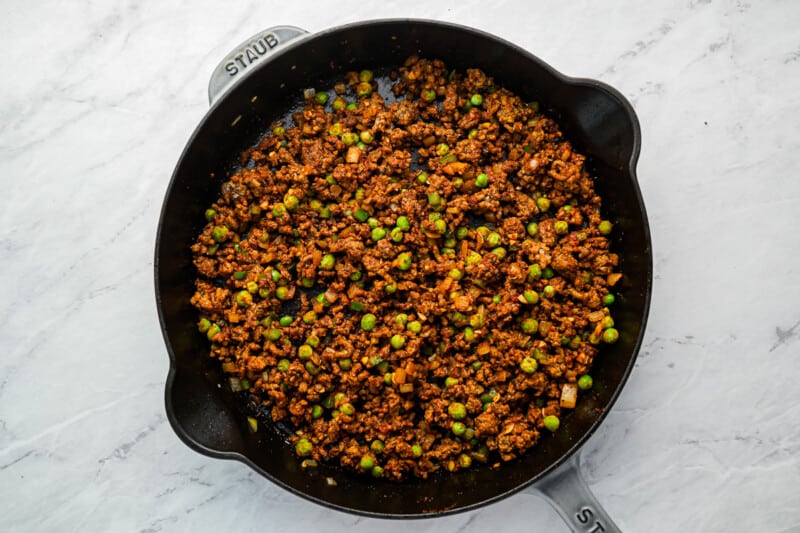 a skillet filled with meat and peas.