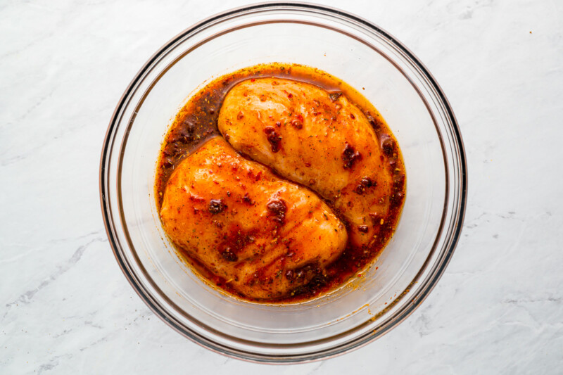 two chicken breasts in a glass dish with sauce.