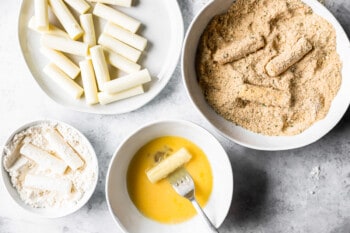 mozzarella sticks at various stages of being dredged through flour, eggs, and breadcrumbs.